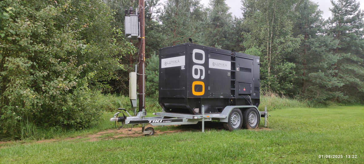 Tume Lumika generaator kaheteljelisel haagisel metsaservas elektriposti kõrval.
